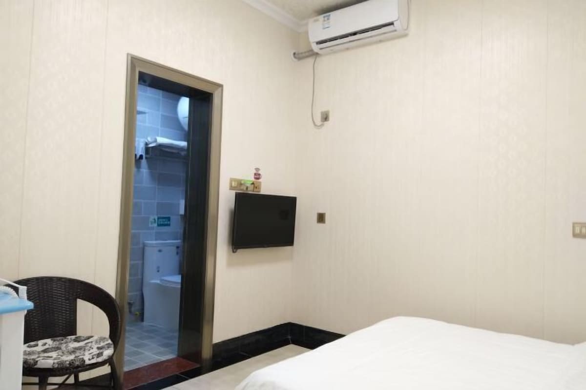 Hotellihuone, jossa on sänky, tuoli, televisio ja ilmastointilaite.
