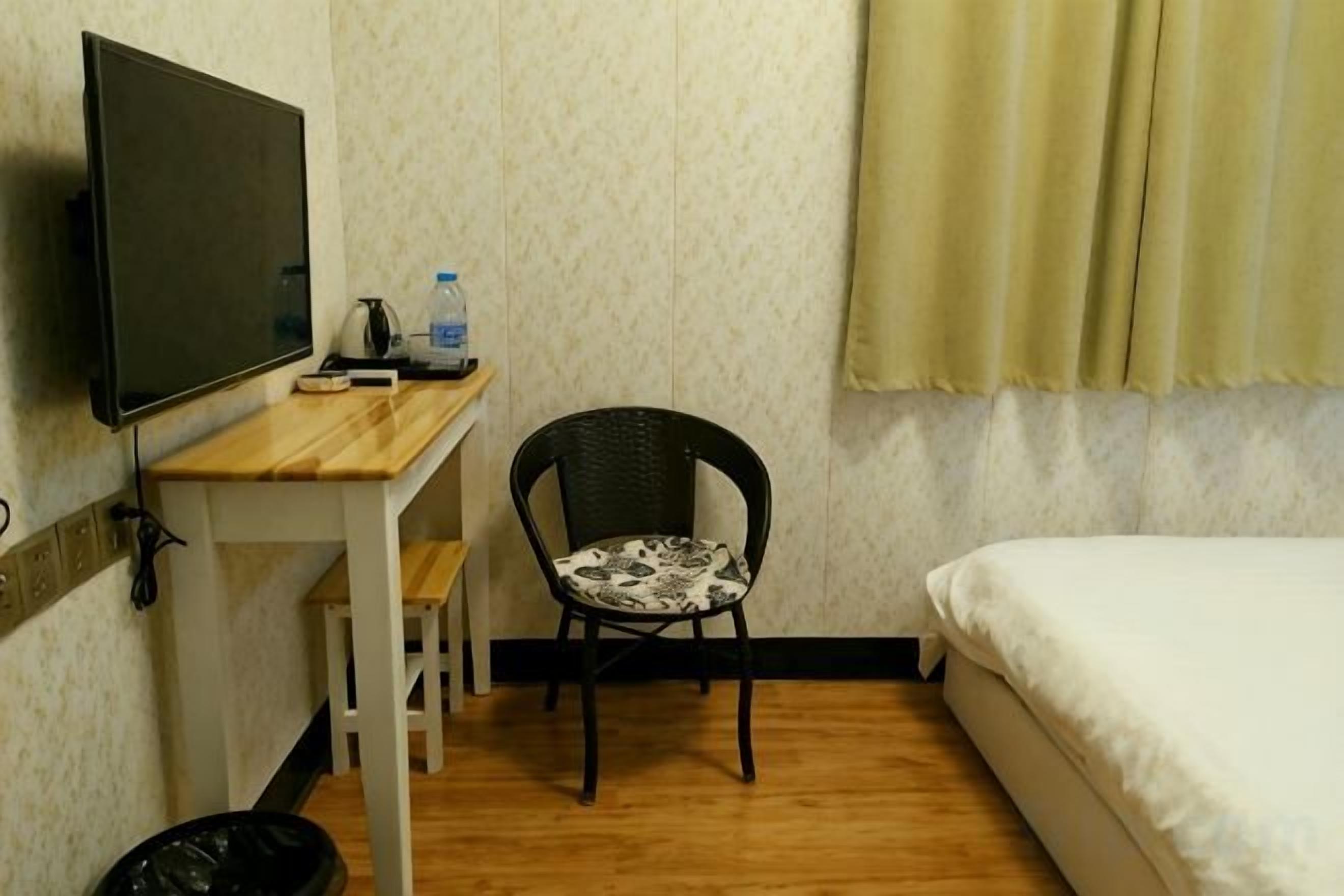 A room with a bed, a desk with a chair, a television, and a trash bin.
