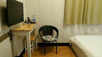 Una habitación con cama, escritorio, silla, televisión y cubo de basura.