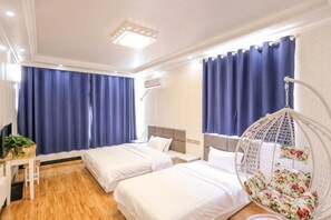 Ein Hotelzimmer mit zwei Betten, einem Schreibtisch, einem Hängesessel und einem großen Fenster mit Vorhängen.