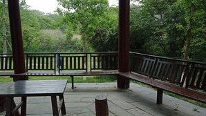 An outdoor wooden deck with benches and tables, surrounded by lush greenery.