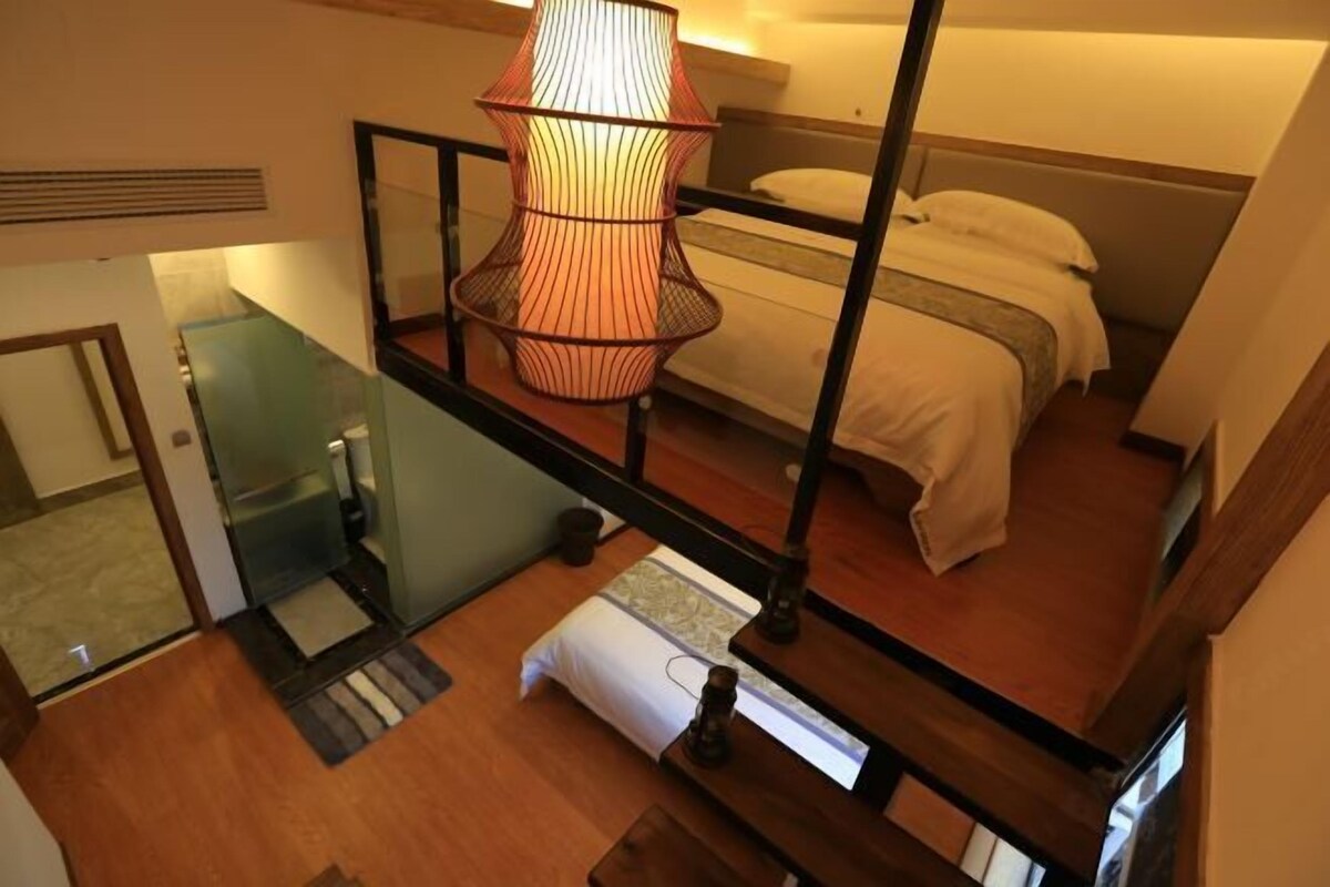 Une chambre à coucher avec un lit, une lampe suspendue, un escalier en bois et une petite table.
