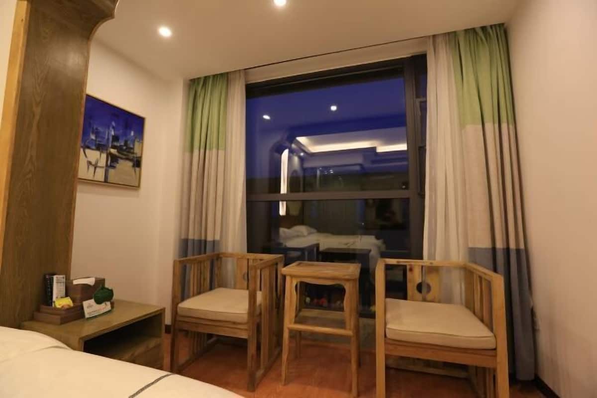Habitación de hotel con un ventanal grande, dos sillas de madera, una mesita y una cama.