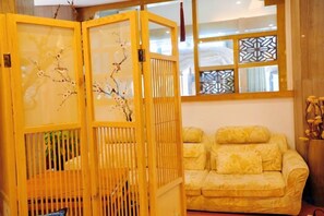 Una habitación con un sofá amarillo, un separador de madera con ramas y un ventanal estampado.