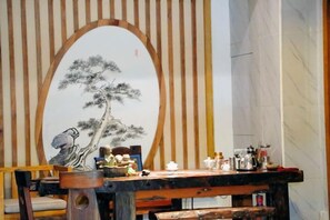 Une pièce au décor intérieur de style japonais traditionnel, comprenant une table en bois sur laquelle sont disposés divers objets, une grande peinture représentant un pin et un paravent shoji.