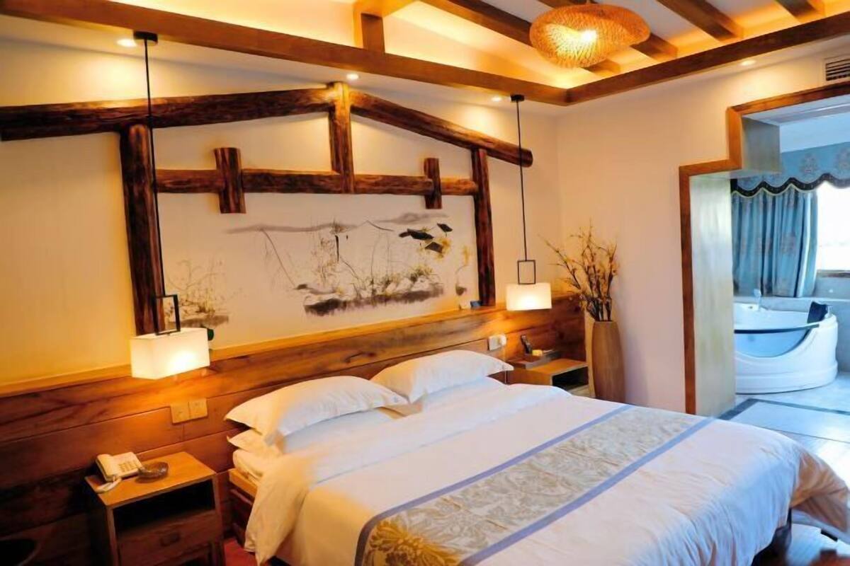 Habitación de hotel con una cama grande, cabecero de madera, lámparas de noche y vista a una piscina.