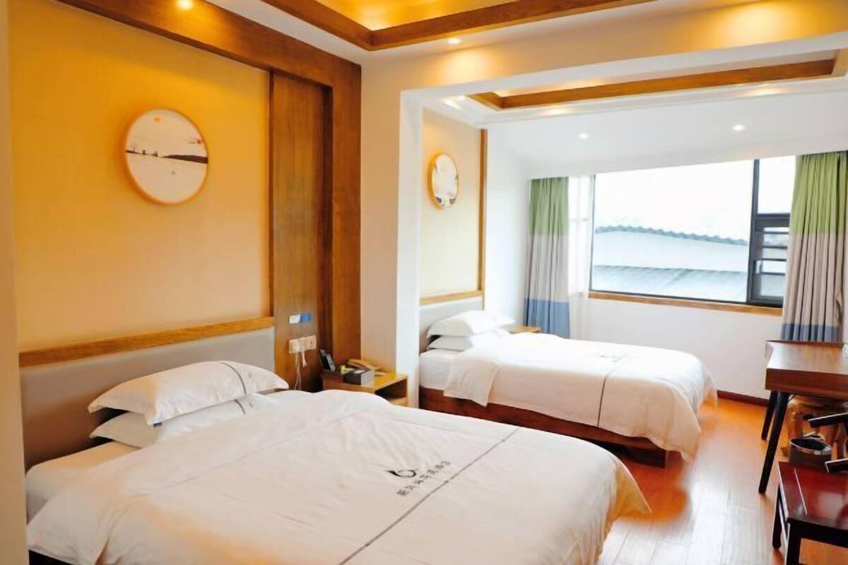 Habitación de hotel con dos camas, un escritorio, una silla, un reloj en la pared y una ventana con cortinas.