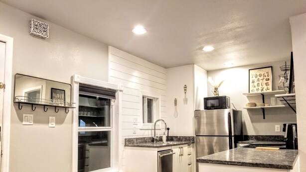A modern kitchen with white cabinetry, a stainless steel refrigerator, a microwave, and a wooden bench.