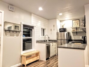 A modern kitchen with white cabinetry, a stainless steel refrigerator, a microwave, and a wooden bench.