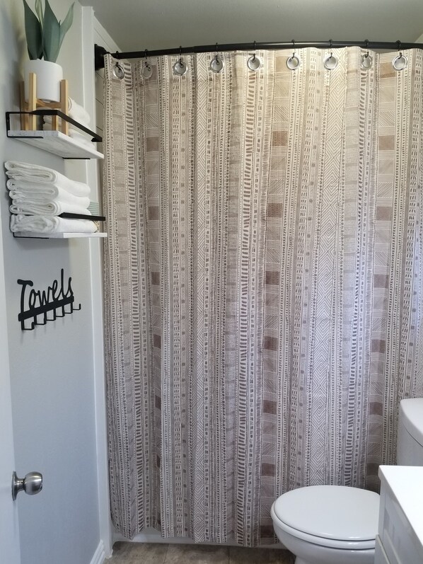 A bathroom with a patterned shower curtain, a toilet, and a towel rack with folded towels.
