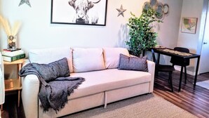 A living room with a sofa, a coffee table, a dining table, and a framed artwork of a bull's head.