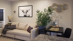 A living room with a sofa, a coffee table, a wall-mounted TV, and decorative items including a plant and framed artwork.
