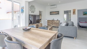 Una sala de estar moderna con una mesa de comedor de madera, un sofá gris y un televisor.