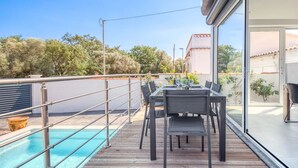 Una terraza de madera con piscina, mobiliario exterior y vistas del paisaje circundante.
