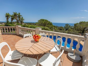 Una mesa de madera redonda con sillas blancas, un frutero y vistas al mar.