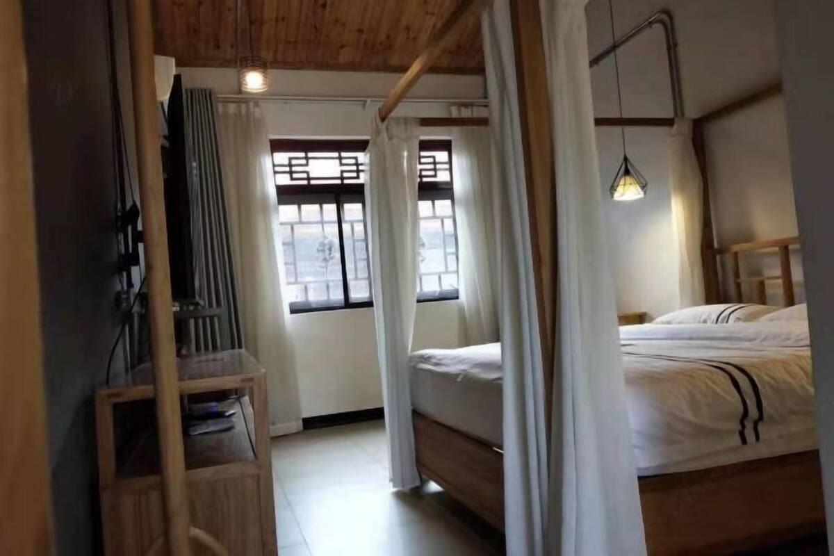 Un dormitorio con cama de madera, mesita de noche, una silla y una ventana con cortinas.
