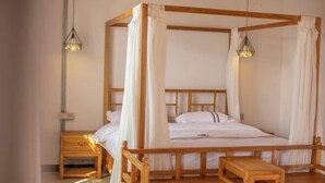Un lit à baldaquin avec une structure en bois et du linge de lit blanc, une table de chevet en bois et une petite table en bois.