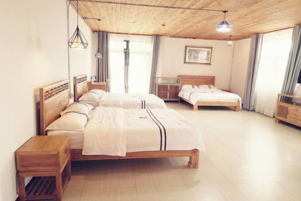 Habitación de hotel con dos camas, cabeceros de madera, suelo de madera y techo con vigas a la vista, además de un ventanal grande con cortinas.