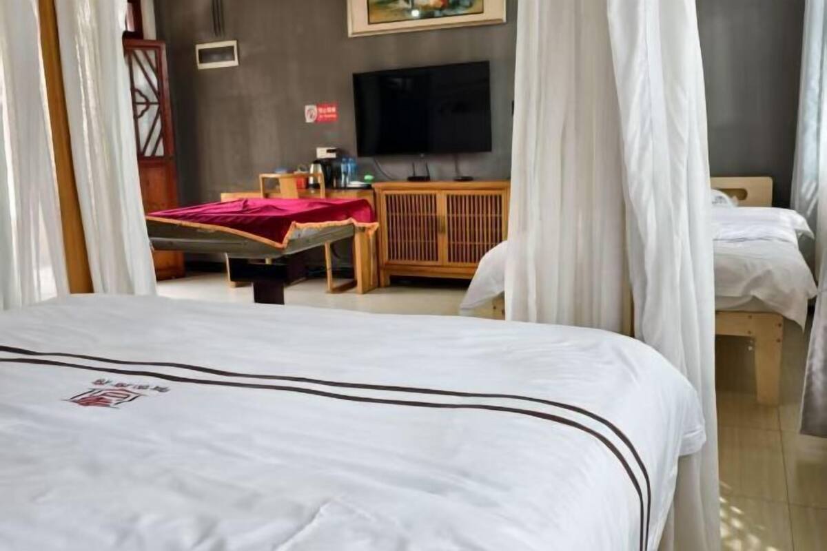 Una habitación de hotel con una cama, televisor, mueble de madera y una colcha roja.