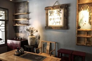 A room with a wooden table, chairs, a vase with dried flowers, shelves, and a wall-mounted sign with Chinese characters. - Youke Susu Hotel (Guiding Yinzhai) (Guiding)