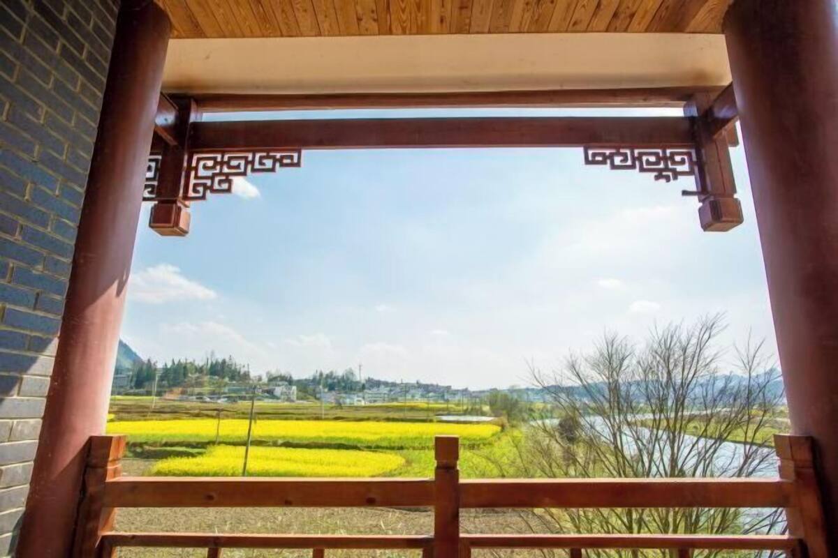 Un balcón de madera con vistas a un paisaje rural, que incluye campos y colinas lejanas.