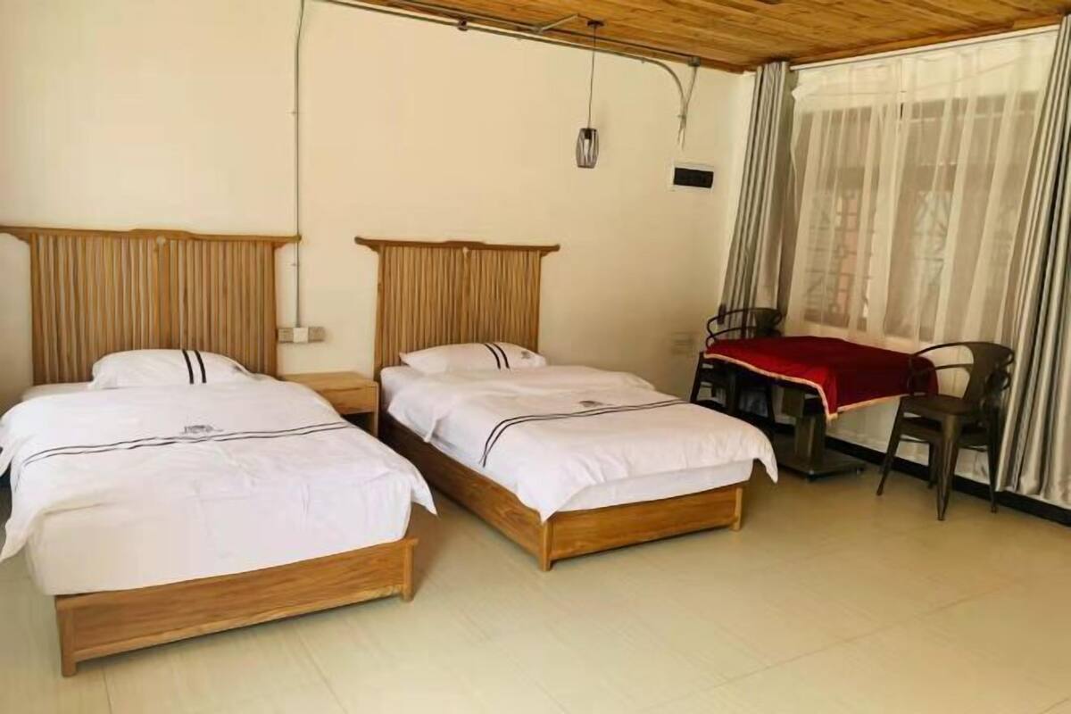 Una habitación con dos camas de madera, un escritorio con silla y una ventana con cortinas.
