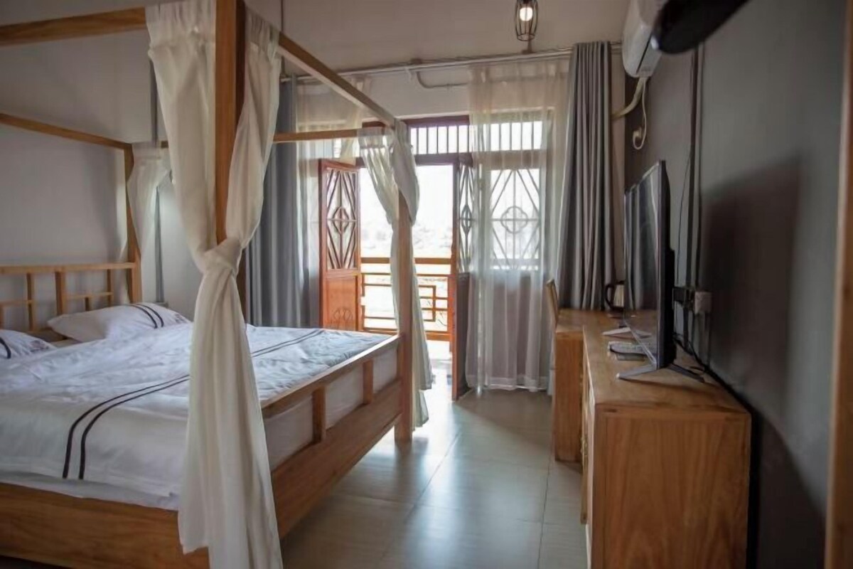 A room with a bed, a desk, a television, and a window with curtains.