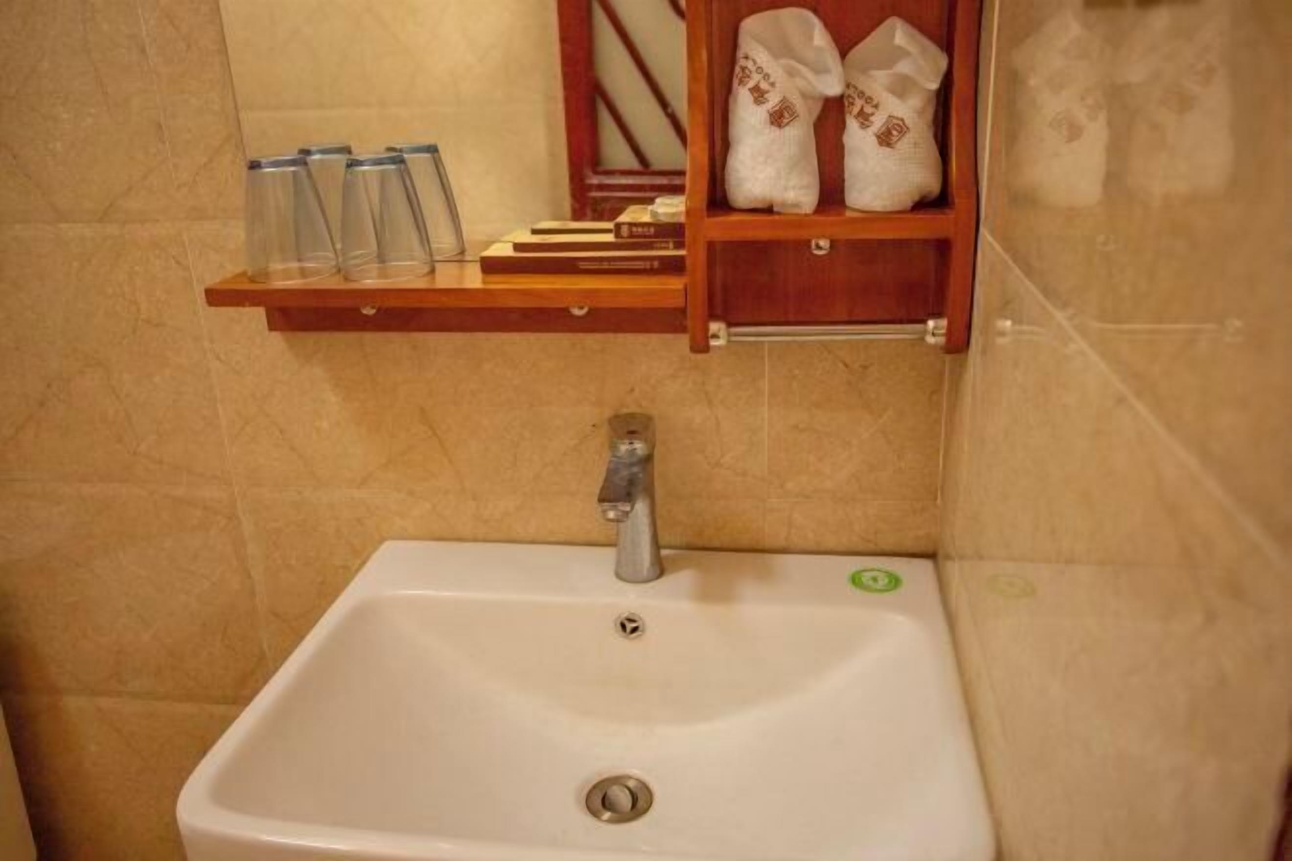 A bathroom with a white sink, a wooden shelf with towels and books, and a tiled wall.