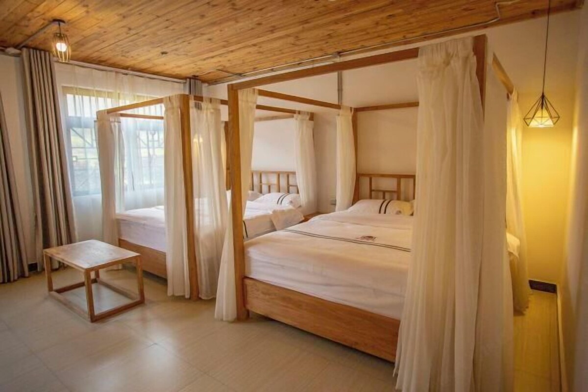 A four-poster bed with white bedding, a wooden bedside table, and a hanging light fixture.
