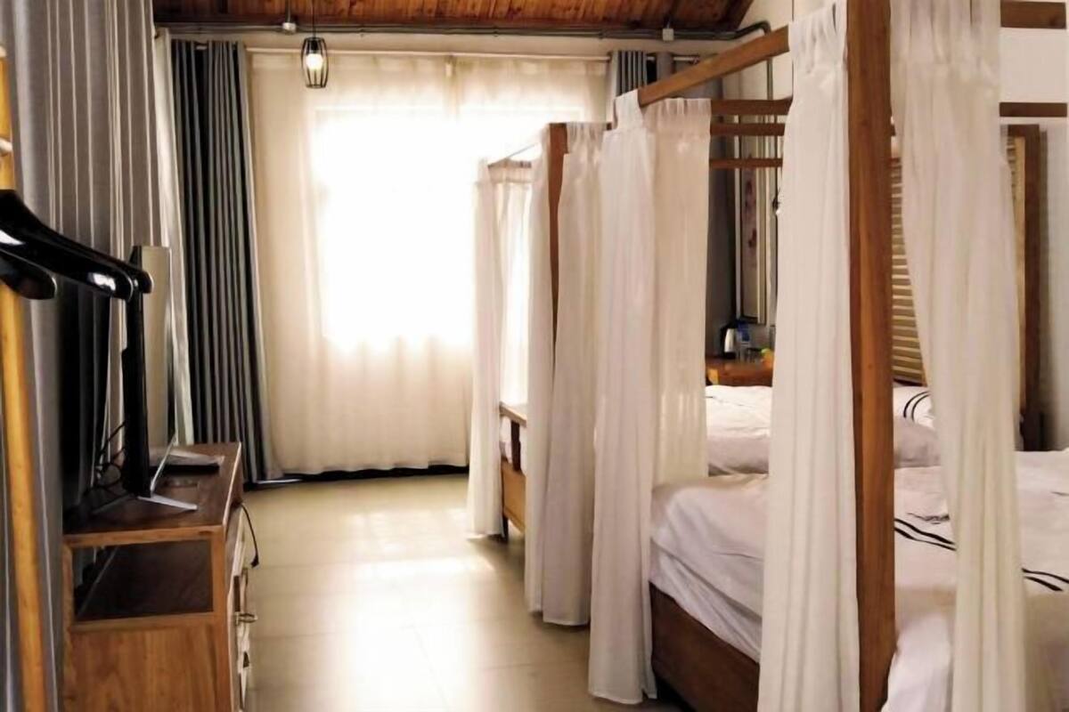 Un dormitorio con estructura de cama de madera, ropa de cama blanca y un escritorio de madera con una silla.