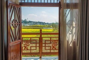 An open wooden gate with geometric patterns, leading to a view of a rural landscape with fields and distant buildings. - Youke Susu Hotel (Guiding Yinzhai) (Guiding)