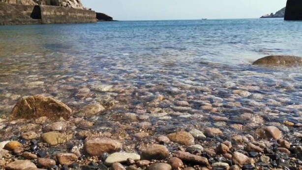 A rocky shoreline with clear water and a distant view of a cliff. - Jingxige Inn (Gouqi Island) (Shengsi)