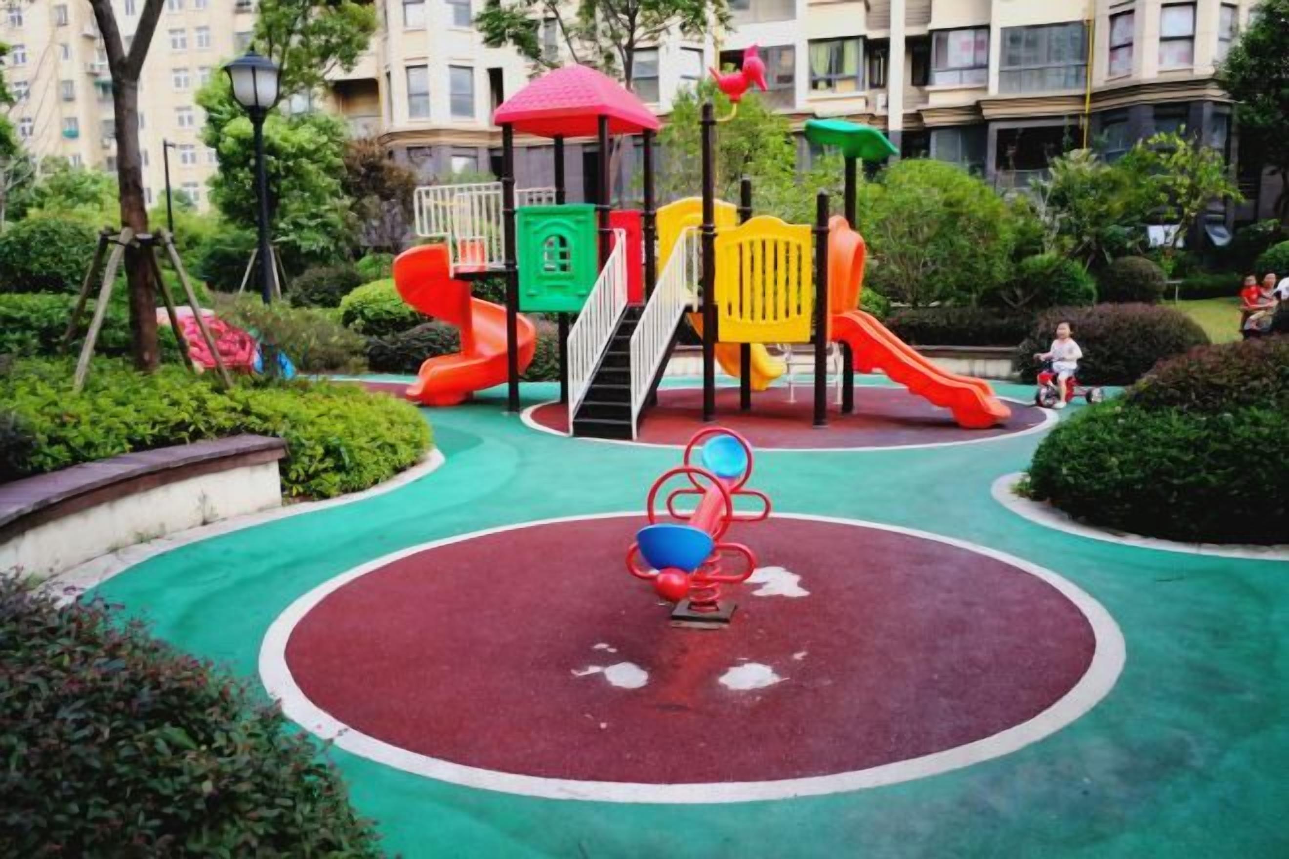 A playground with a red slide, yellow and green climbing structures, and a red and blue merry-go-round.