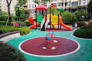 A playground with a red slide, yellow and green climbing structures, and a red and blue merry-go-round. - Youxiang Hotel (Wenzhou)