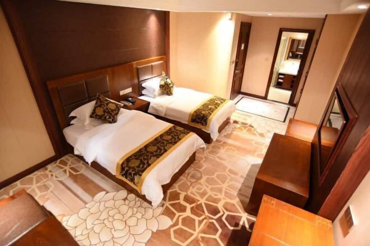 A hotel room with two beds, a wooden headboard, a patterned carpet, and a mirror on the wall.