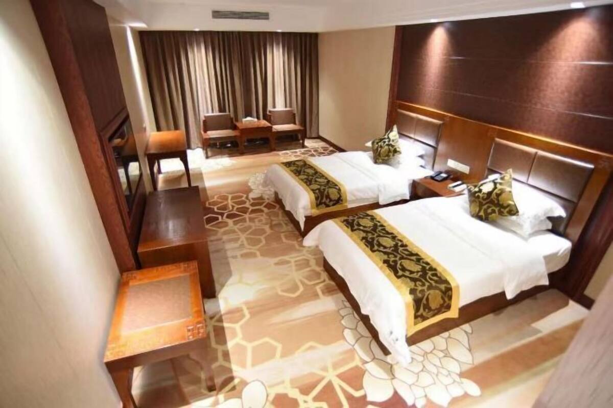 A hotel room with two beds, a sitting area with chairs, a small table, and a patterned carpet.