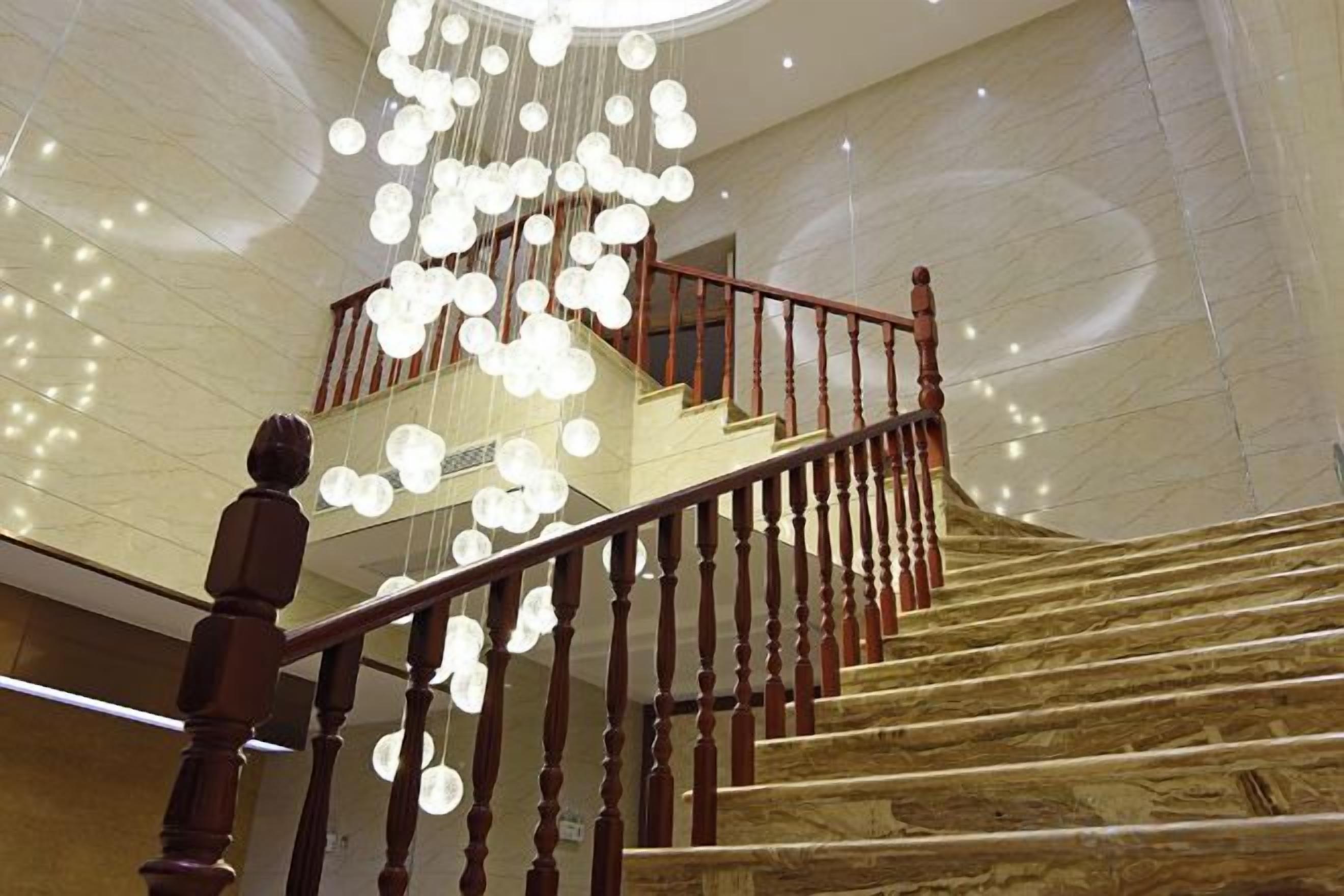 A grand staircase with a wooden handrail and a chandelier with multiple light fixtures.