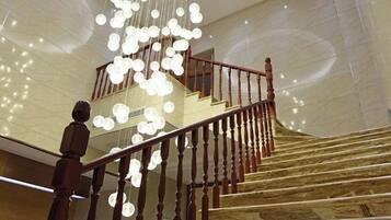 A grand staircase with a wooden handrail and a chandelier with multiple light fixtures.