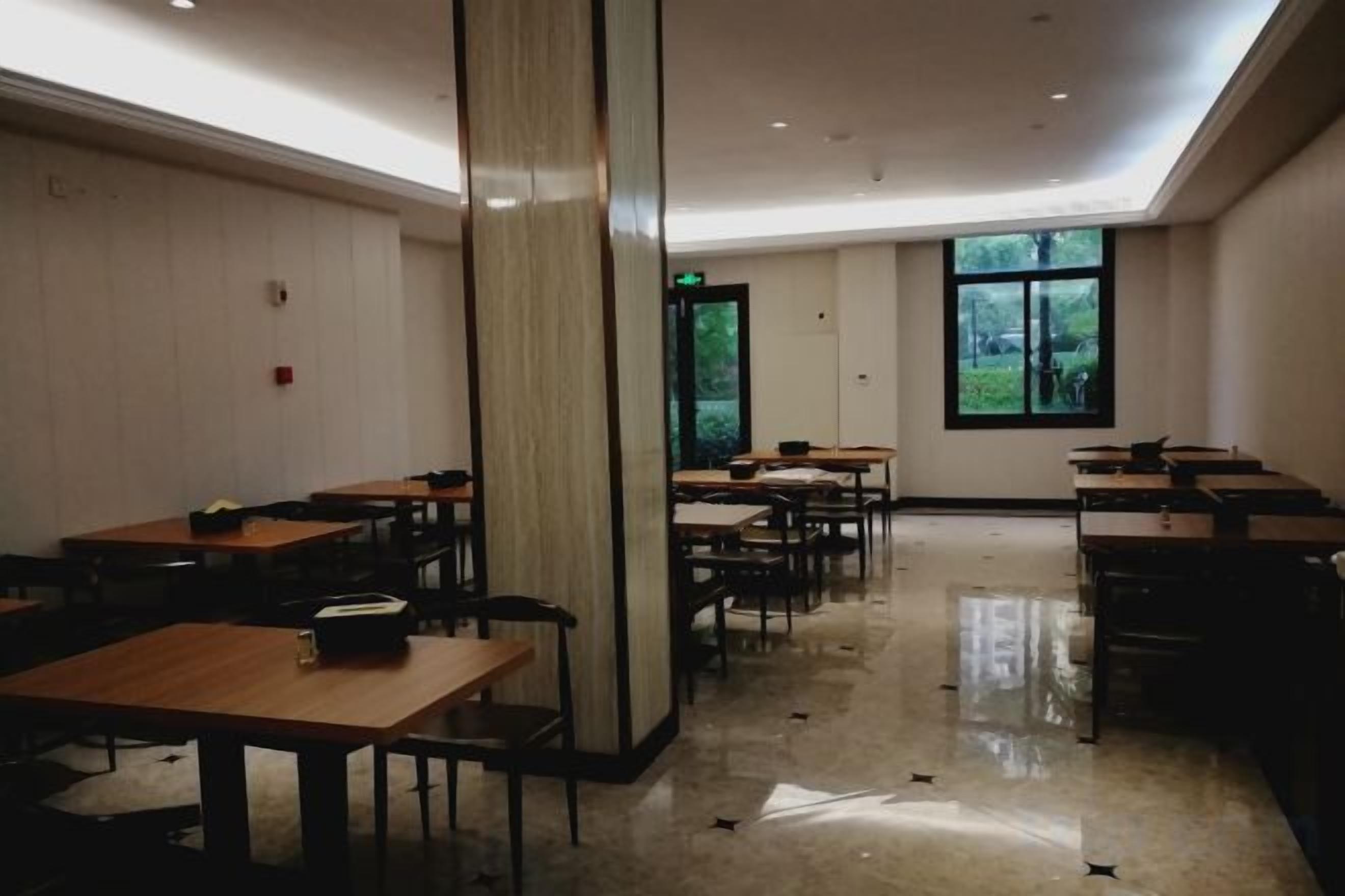 A spacious room with multiple tables and chairs, a large pillar, and a window providing a view of greenery outside.