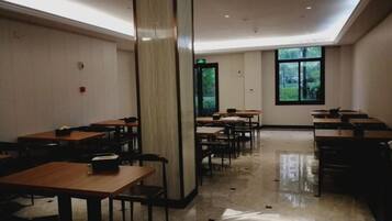 A spacious room with multiple tables and chairs, a large pillar, and a window providing a view of greenery outside.