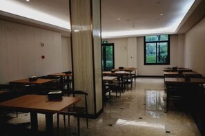 A spacious room with multiple tables and chairs, a large pillar, and a window providing a view of greenery outside. - Youxiang Hotel (Wenzhou)