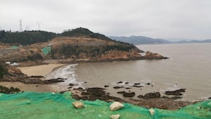 Un paysage côtier avec une plage, une côte rocheuse et des montagnes à l’horizon.