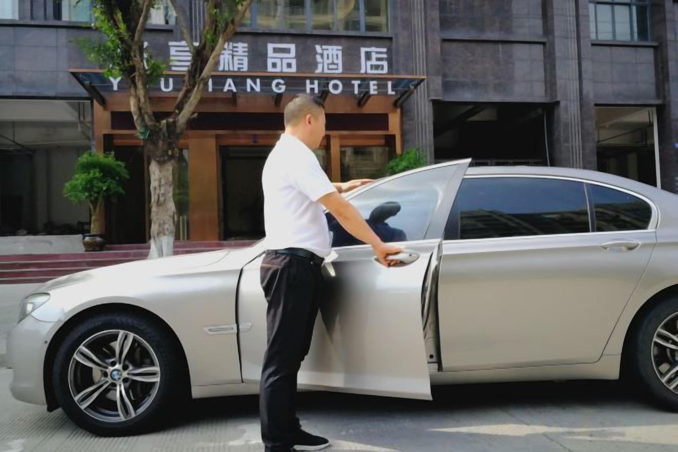 Ein Mann öffnet die Autotür vor einem Hotel, dessen Schild 'YIYANG HOTEL' zeigt.