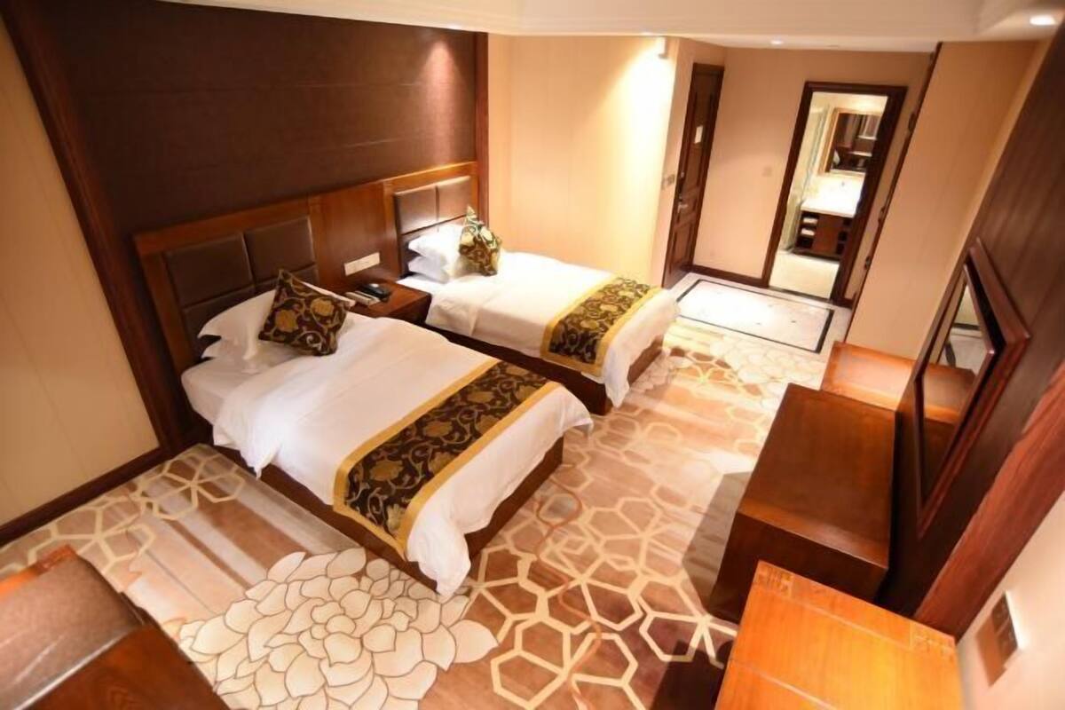 A hotel room with two beds, a wooden headboard, a patterned carpet, and a mirror on the wall.