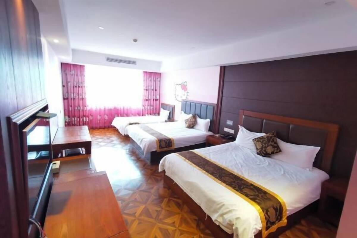 A hotel room with two beds, a wooden desk, and a large window with pink curtains.