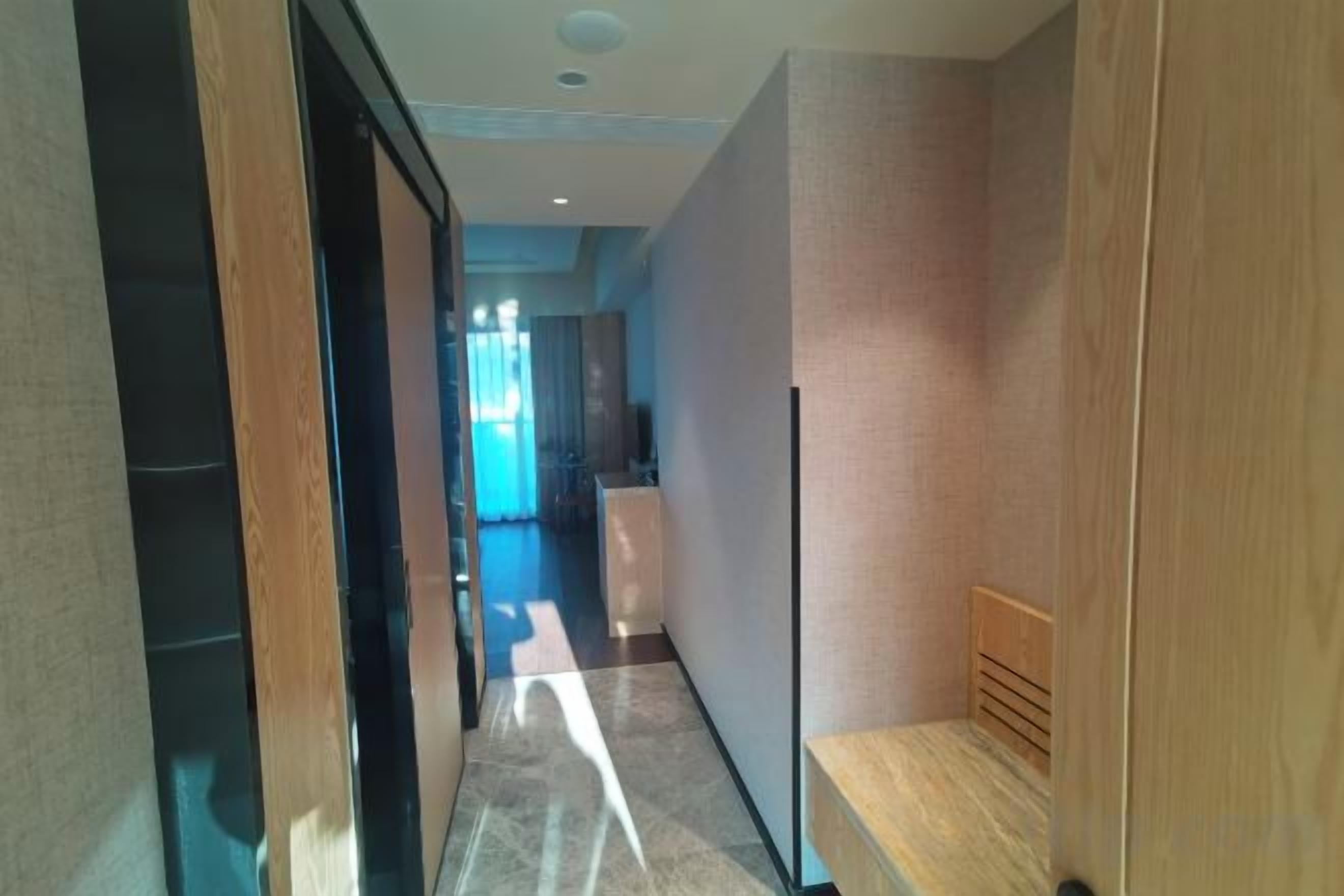 A hallway with a wooden bench, a door, and a view into a room with a window.