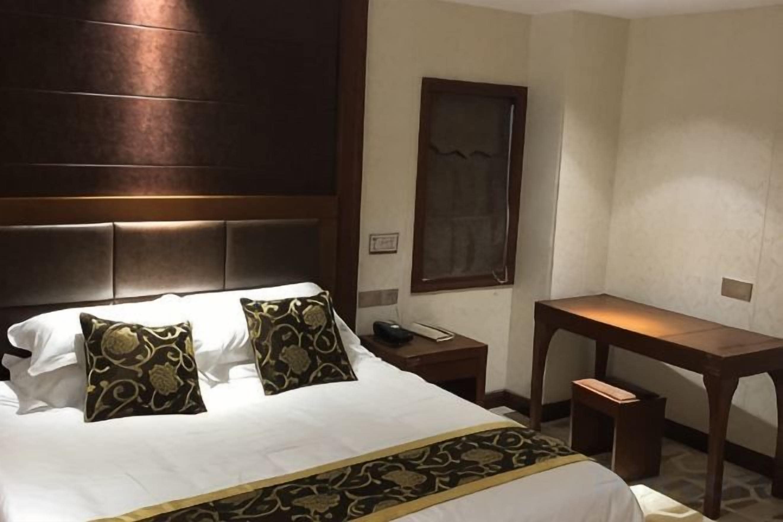 Une chambre d’hôtel avec un grand lit, deux coussins décoratifs, une table de chevet avec un téléphone, un bureau et une chaise.