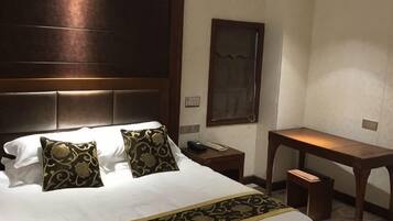 Une chambre d’hôtel avec un grand lit, deux coussins décoratifs, une table de chevet avec un téléphone, un bureau et une chaise.