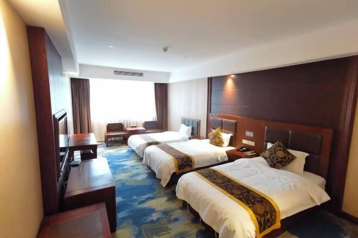 A hotel room with two beds, a desk, and a view of the outdoors.