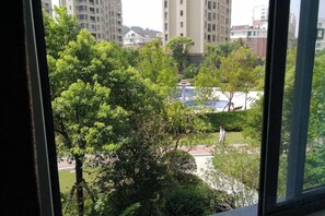 A view through a window of a park with trees and a building in the background. - Youxiang Hotel (Wenzhou)
